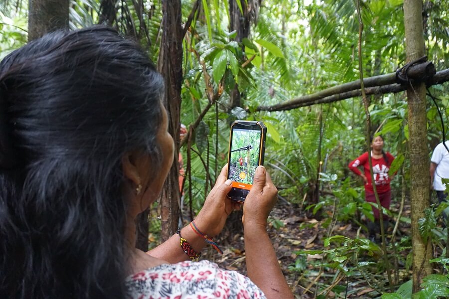 Uma foto de uma mulher tirando uma foto da atividade humana em uma floresta usando o aplicativo Mapeo em seu smartphone.
