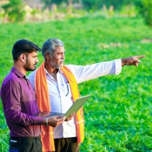 A photo of two Indian men standing in a field looking tablet.