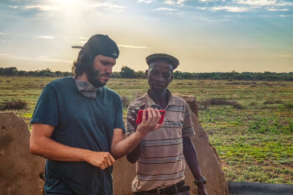 Two men standing in a field looking at a cell phone.
