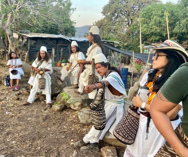 A group of indigenous Colombians wearing traditional Arhuacos dress, stand near ground that is being prepped to grow cacao.